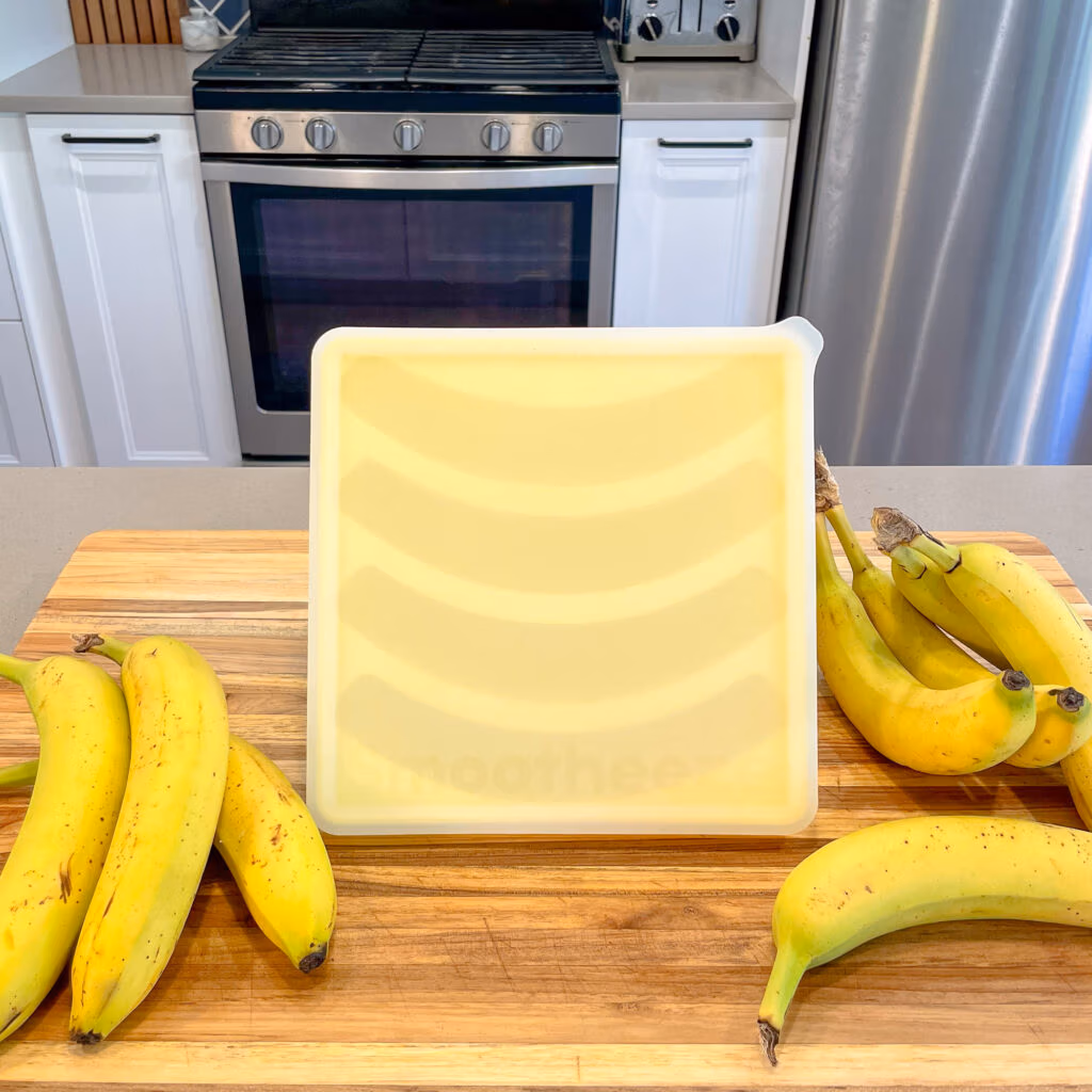 Smootheeze banana freezer tray laying on the counter next to unpeeled bananas