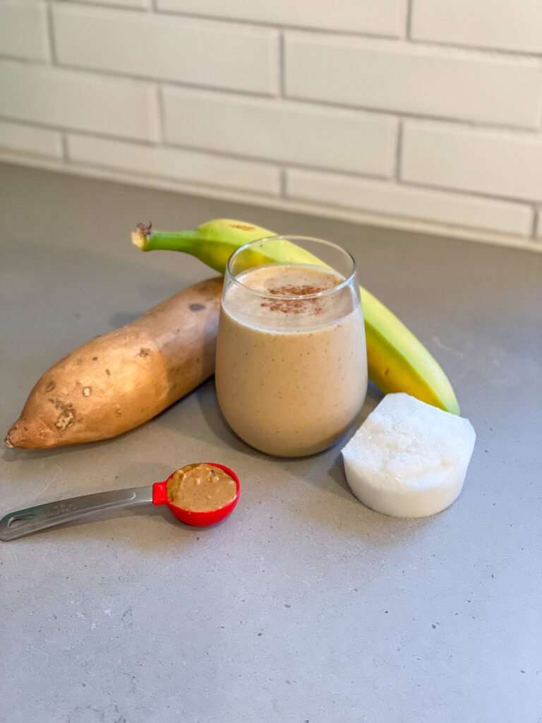 Smoothie in a glass surrounded by ingredients including sweet potato, banana, and coconut milk