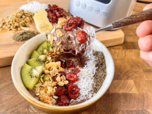 A smoothie bowl made from frozen fruit topped with coconut, granola, kiwi, and chia seeds, positioned on the counter.