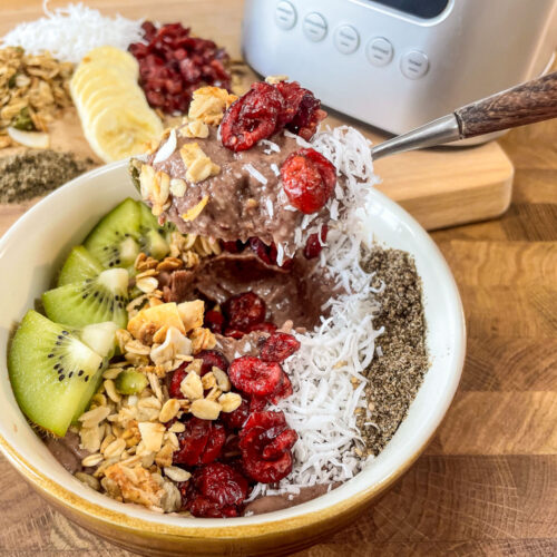 A smoothie bowl made from frozen fruit topped with coconut, granola, kiwi, and chia seeds, positioned on the counter.