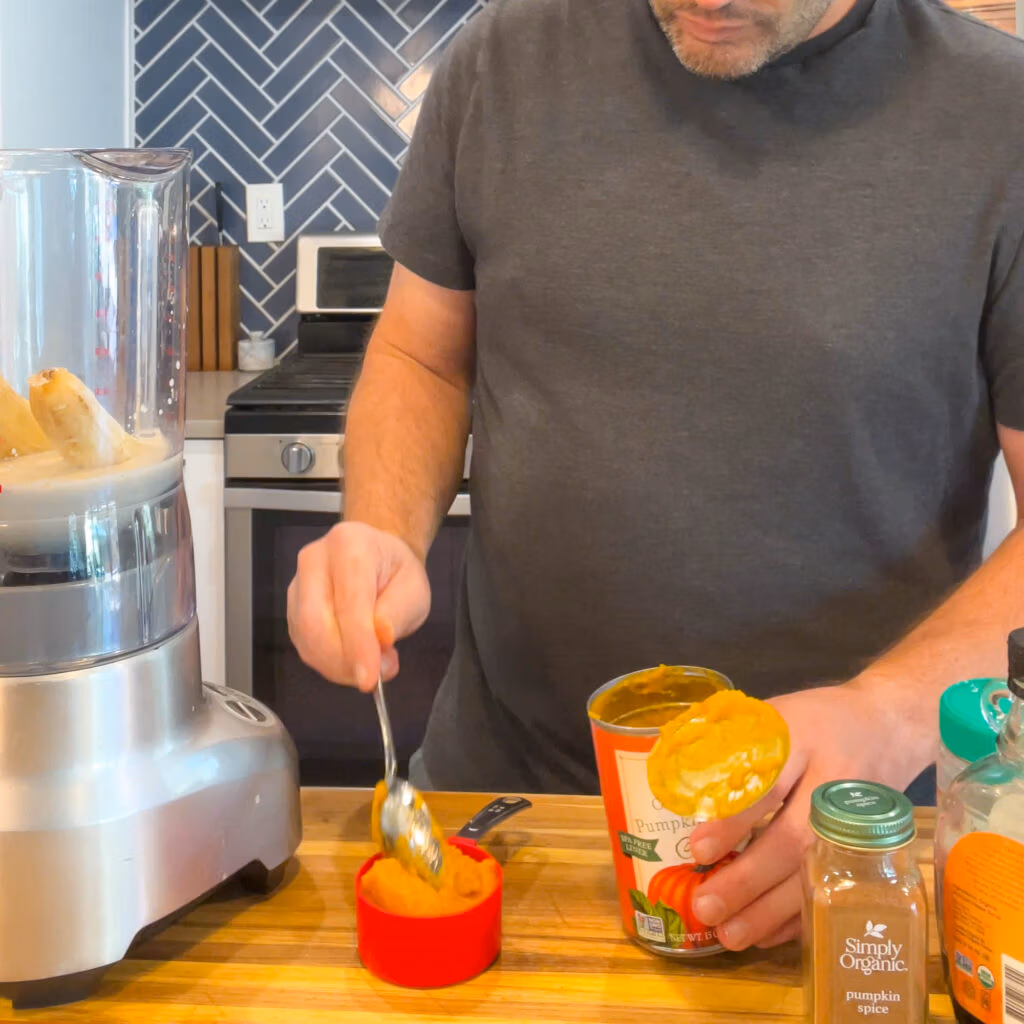Adding pumpkin puree to a measuring cup to add to the blender