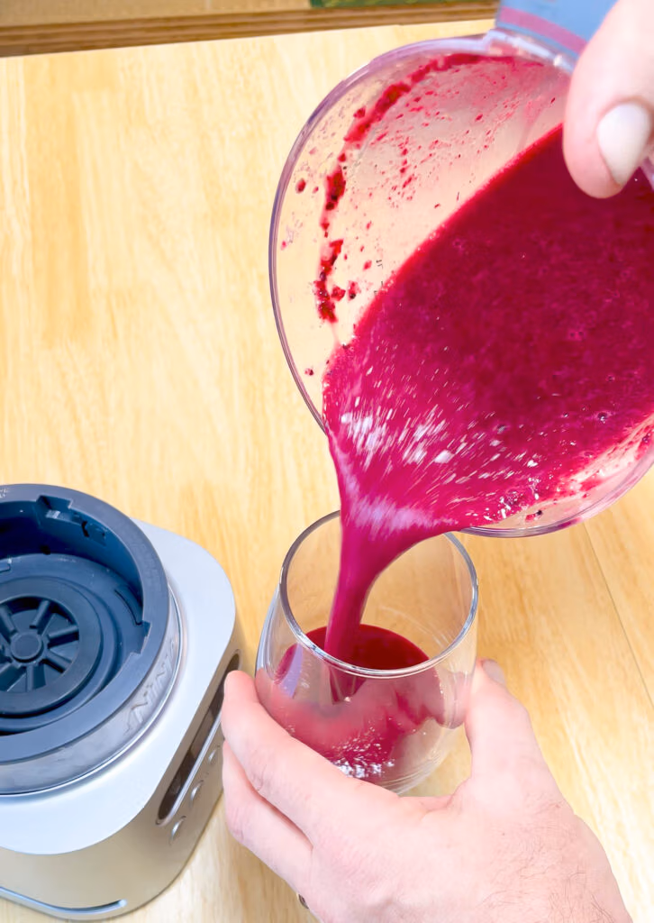 Red beet smoothie blended and being poured into a glass.